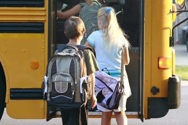 Kids boarding a yellow school bus with backpacks.